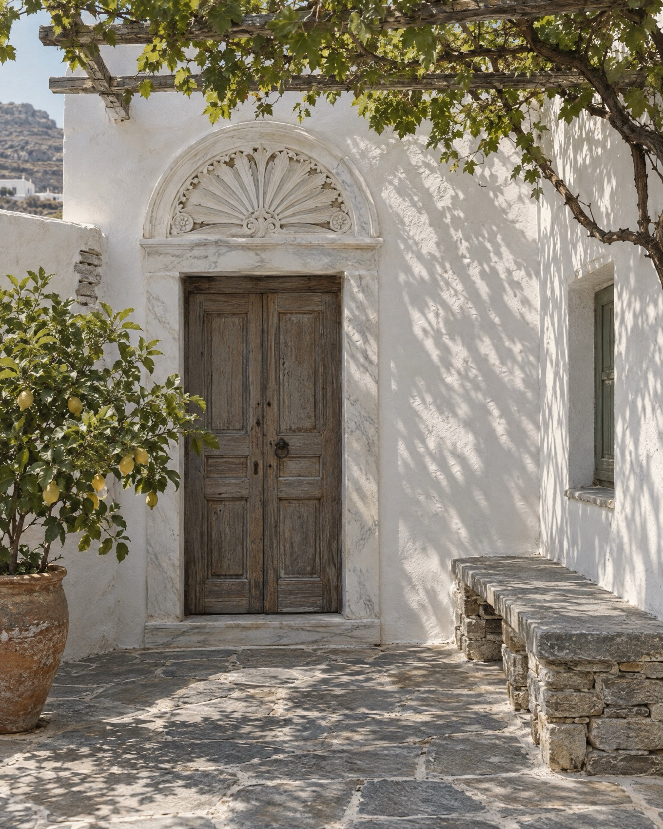 Σκαλιστός μαρμάρινος φεγγίτης πάνω από παλιά ξύλινη πόρτα, σε αυλή με λεμονιά, Τήνος